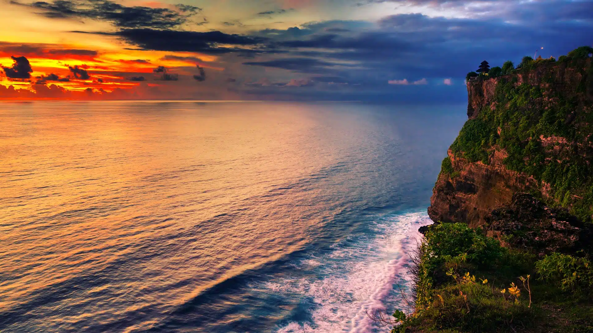A scenic bird's-eye view of a dramatic cliffside coastline during a vibrant golden sunset over the calm ocean waters.