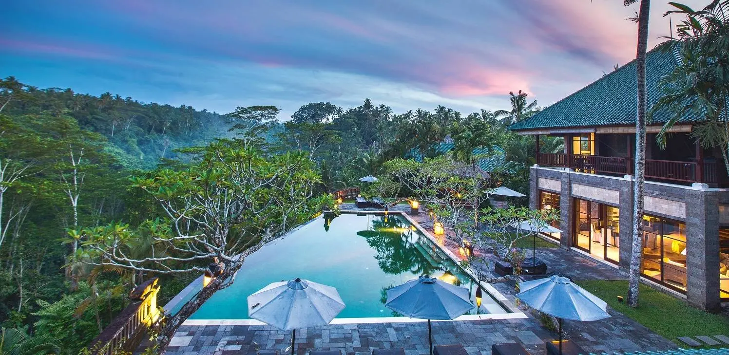 Luxury Balinese villa with an infinity pool overlooking a tropical jungle valley at twilight with a colorful sunset sky.