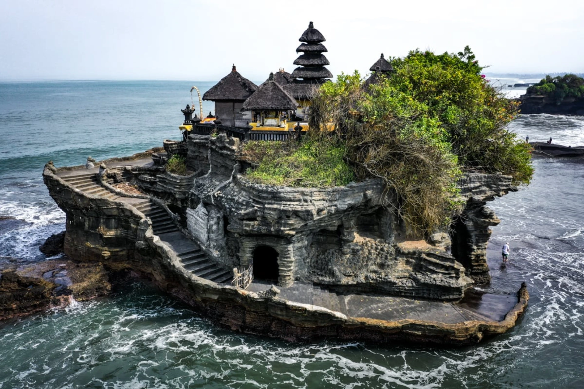 High-angle view of the iconic Tanah Lot Temple in Bali, built on a unique offshore rock formation surrounded by crashing ocean waves