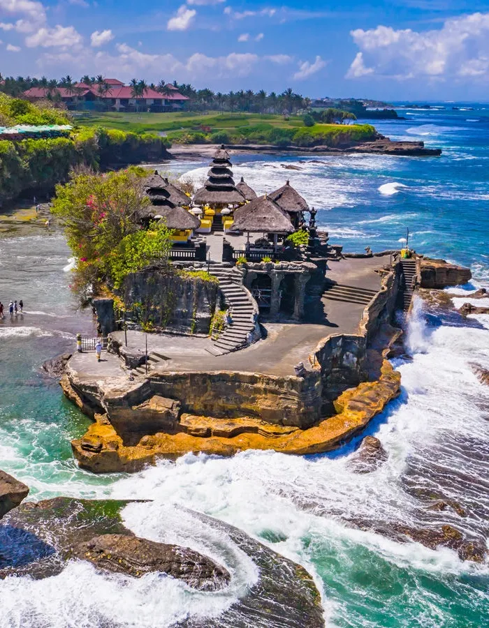 High-angle view of the iconic Tanah Lot Temple in Bali, built on a unique offshore rock formation surrounded by crashing ocean waves