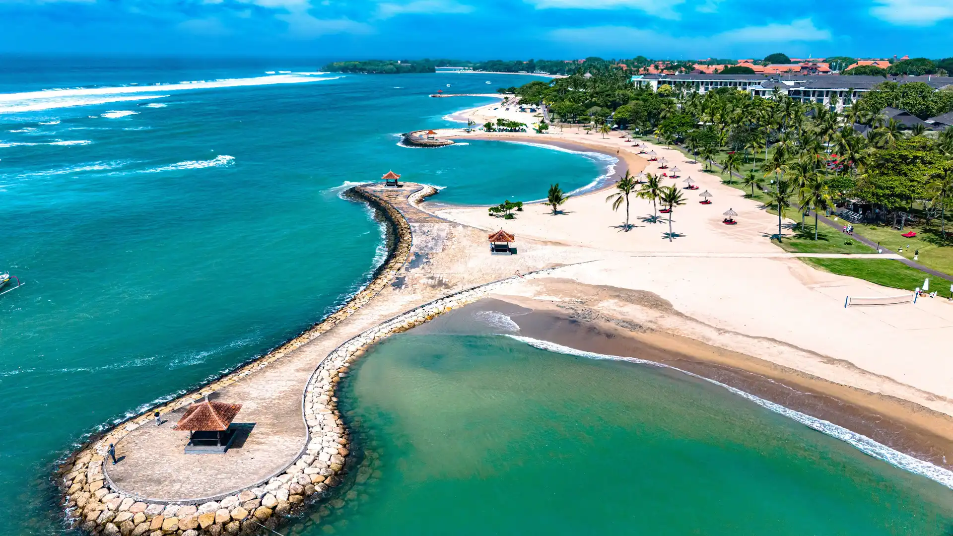 Aerial view of a luxury beachfront resort enclave in Bali with pristine white sand beaches and turquoise ocean water