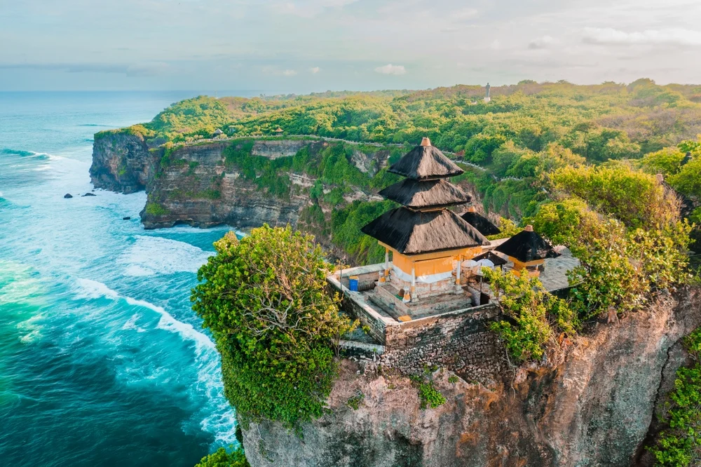Aerial view of the ancient Uluwatu Temple perched on a shear cliff edge in Bali, overlooking the Indian Ocean at sunset
